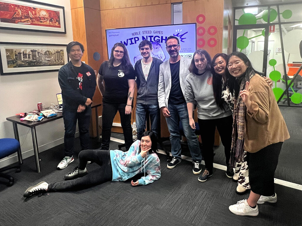 A group photo of all the presenters and organisers in front of the WIP Night screen. From left to right: Jason, Dom, Evan, David, Liv, Christine, Ann and lying at the ground, Rose.