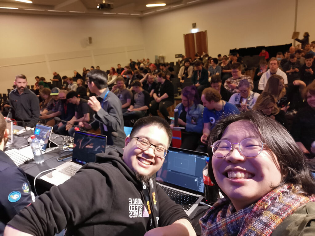 A selfie of Grant and Ann in front of the Survivor Game Jam crowd.