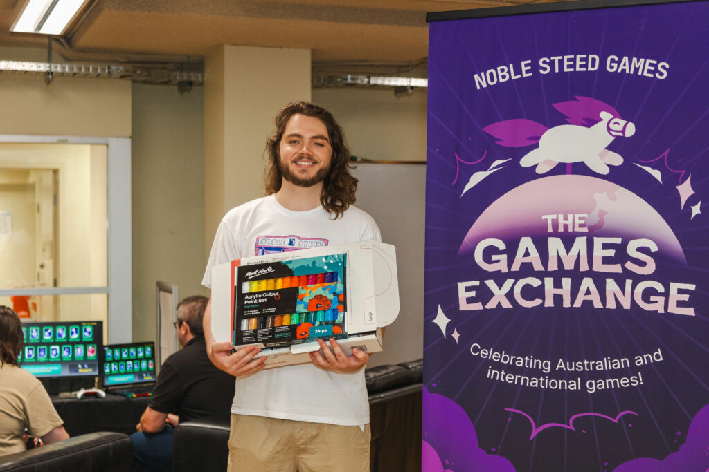 Here's Ethan, the first person to win Bingo, with a full set of art supplies donated by Pat Naoum! 
(Whose game was also involved!) He is standing with the art supplies in his hand, next to the Games Exchange pull up banner.